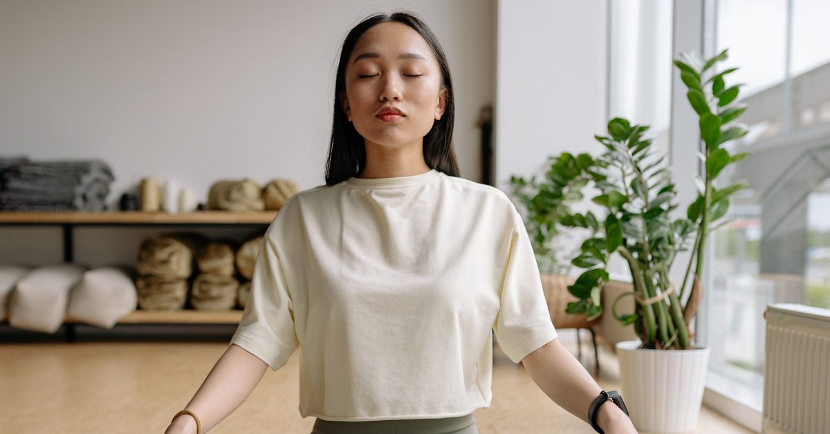 Achtsamkeitsmeditation: die geführte Sitzpraxis Frau sitzt mit geschlossenen Augen im Schneidersitz auf einer Matte, Sinnbild für Achtsamkeitsmeditation im Sitzen