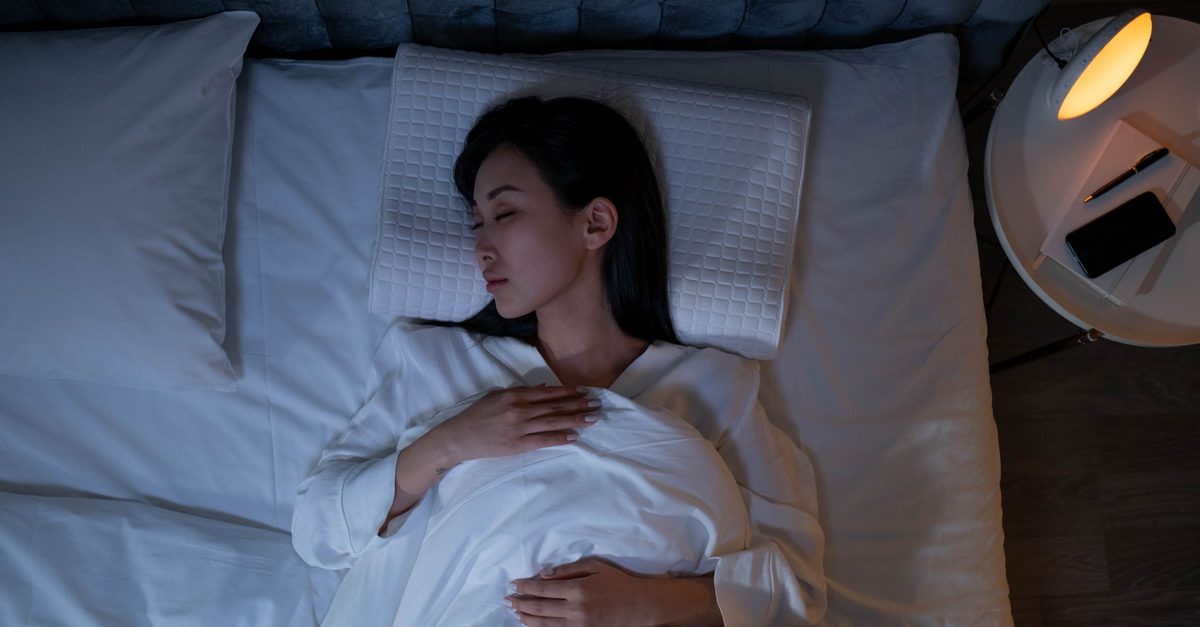 Frau schläft friedlich im abgedunkelten Schlafzimmer bei gedämmtem Licht, Sinnbild für eine Meditation zum Einschlafen