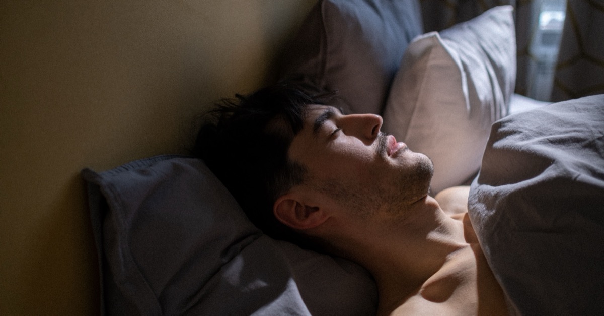 Mundatmung im Schlaf erkennen Mann schläft morgens mit leicht geöffnetem Mund im Bett, Sinnbild für Mundatmung im Schlaf