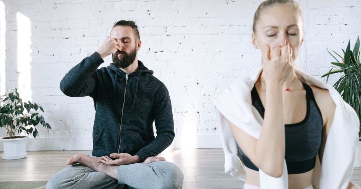 Paar sitzt im Schneidersitz und übt gemeinsam eine ruhige Pranayama-Atemtechnik