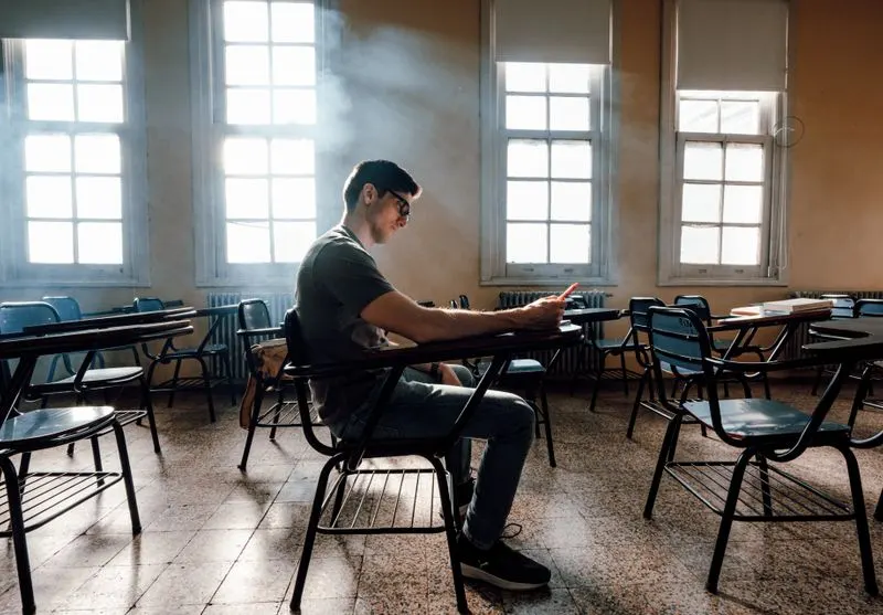 Student lernt allein und konzentriert in einem sonnendurchfluteten, leeren Klassenraum vor der Prüfung