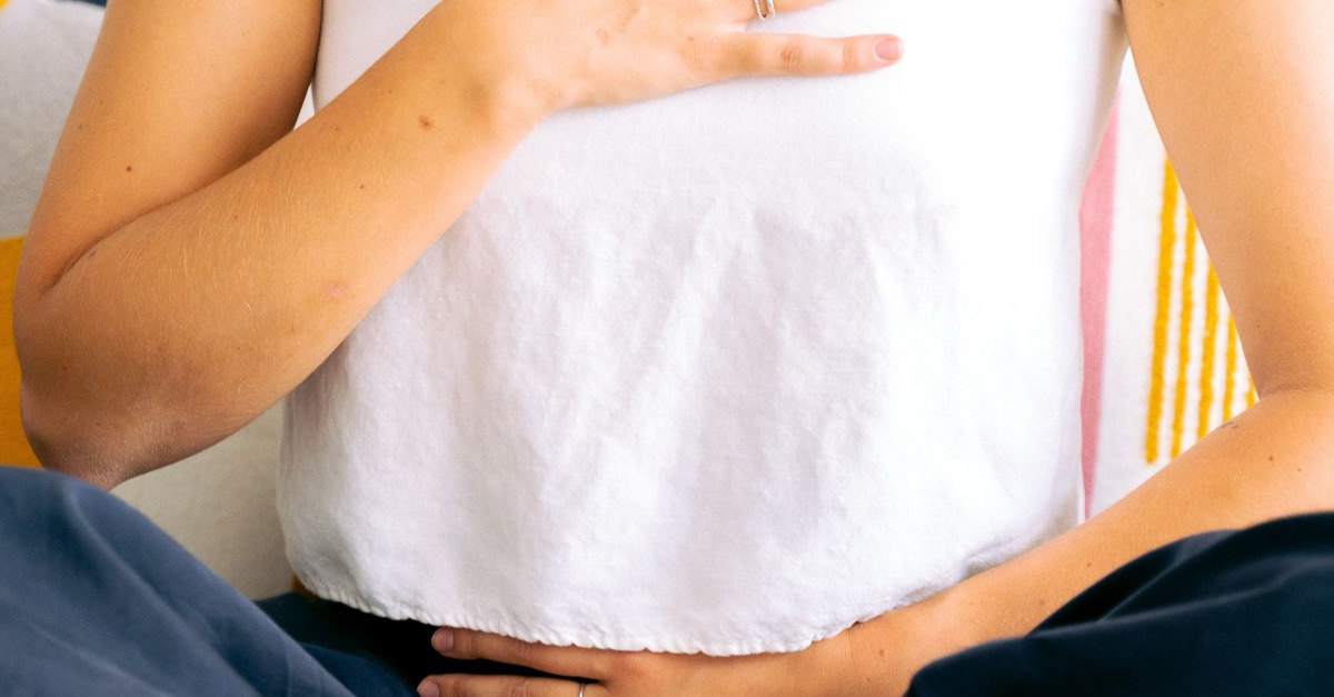 Frau im Schneidersitz legt bewusst eine Hand auf die Brust und eine Hand auf den Bauch, Sinnbild für den willentlichen Zugriff des somatischen Nervensystems