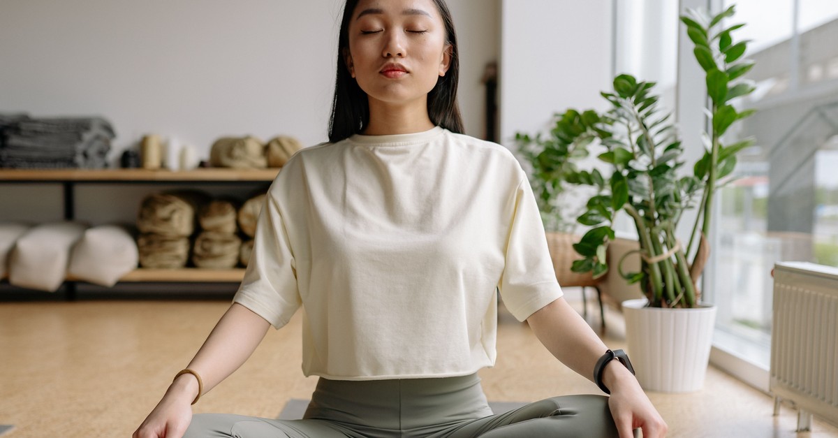 Vipassana Meditation zuhause üben Frau sitzt mit geschlossenen Augen im Schneidersitz und übt Vipassana Meditation zuhause